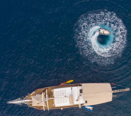 Aerial view of a gulet sailing on the Fethiye to Kekova and Back Blue Cruise, with a speedboat creating a perfect circle in the turquoise waters.