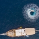 Aerial view of a gulet sailing on the Fethiye to Kekova and Back Blue Cruise, with a speedboat creating a perfect circle in the turquoise waters.