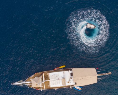 Aerial view of a gulet sailing on the Fethiye to Kekova and Back Blue Cruise, with a speedboat creating a perfect circle in the turquoise waters.