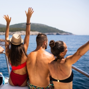 Group of young adults enjoying the sun and sea breeze on deck during the Olympos to Fethiye gulet cruise, raising their hands in excitement