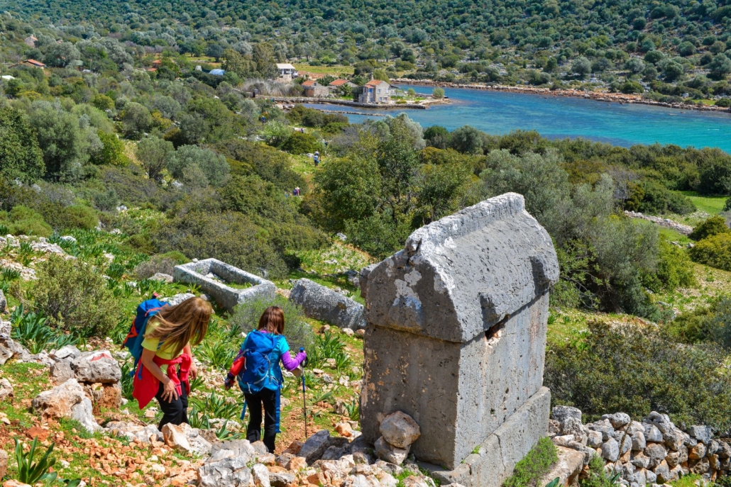 Hikers trekking along the Lycian Way, passing ancient Lycian rock tombs with a stunning view of the Mediterranean coastline in the background.