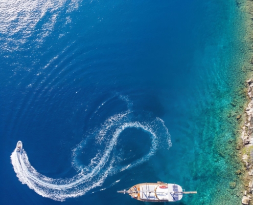 Aerial view of a gulet anchored near the coast with a tender boat making a circular trail during the Kemer to Kekova and Back gulet cruise