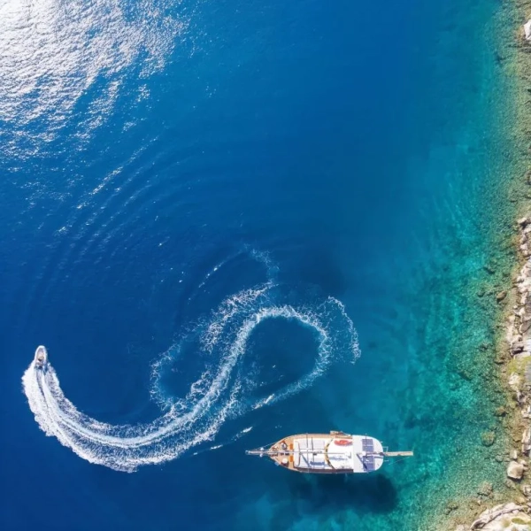 Aerial view of a gulet anchored near the coast with a tender boat making a circular trail during the Kemer to Kekova and Back gulet cruise