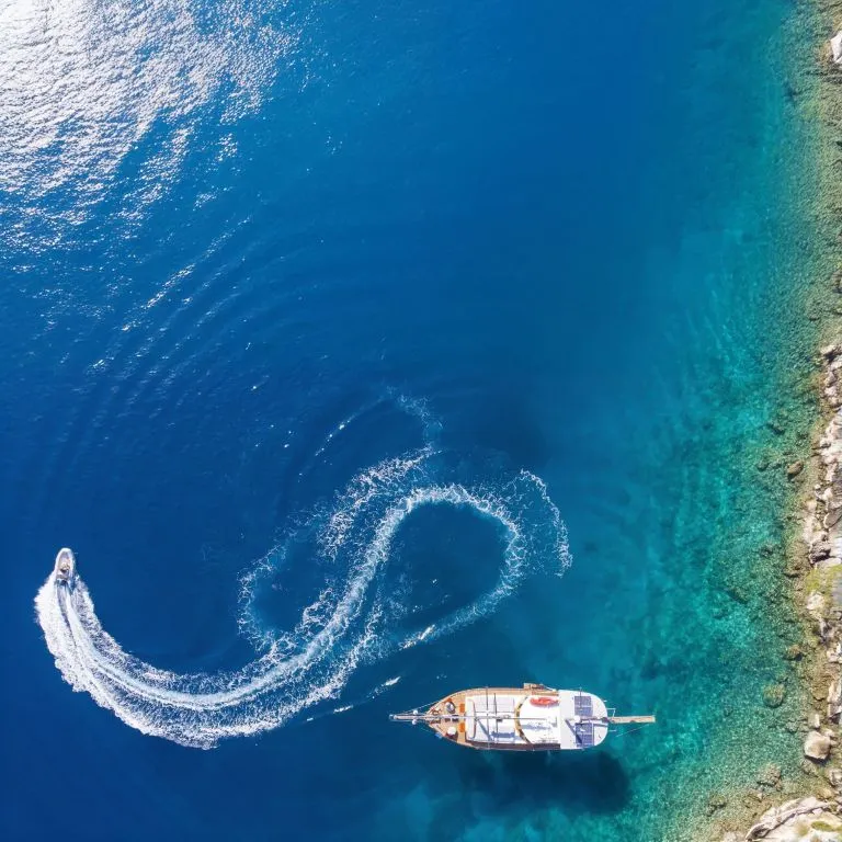 Aerial view of a gulet anchored near the coast with a tender boat making a circular trail during the Kemer to Kekova and Back gulet cruise
