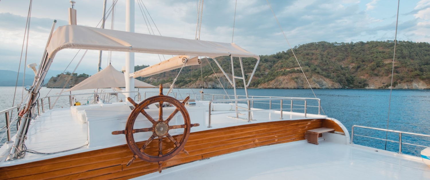 View of a traditional gulet’s upper deck and steering wheel during a Sail Turkey blue cruise, anchored in a scenic Mediterranean bay