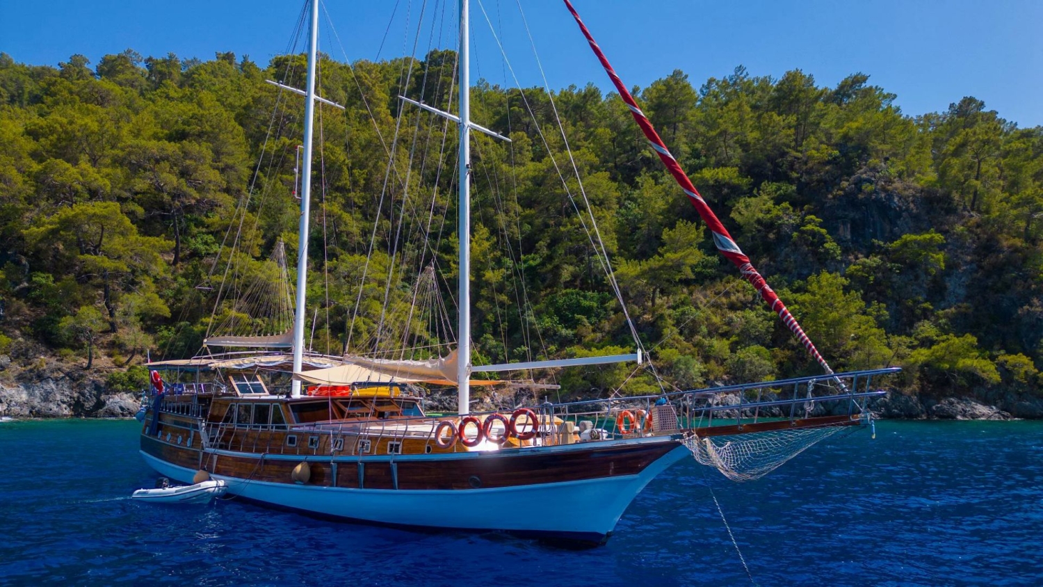 Traditional Turkish gulet anchored in a secluded bay during a Sail Turkey blue cruise, surrounded by pine forests and clear blue water